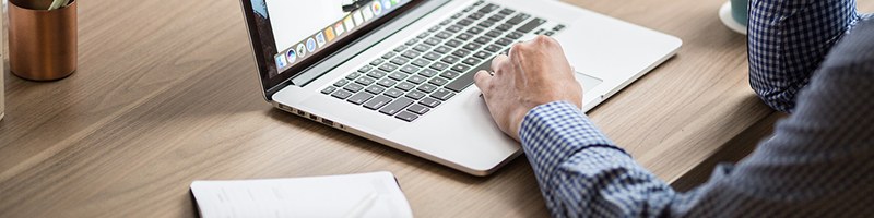 Bild: Ausschnitt einer Person an einem Schreibtisch mit Laptop // Photo: Detail of a person with a laptop at a desk