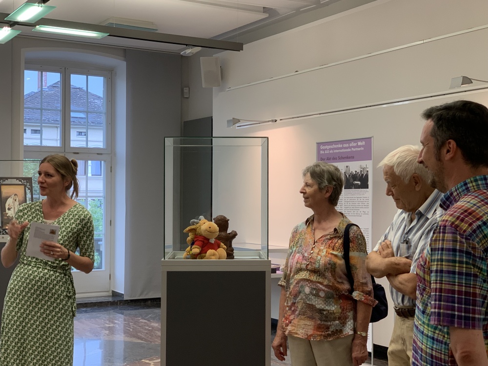 Ausstellungsbesucher stehen neben einer Vitrine mit Maskottchen