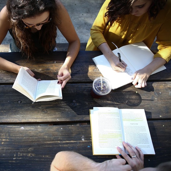 Persons sitting at a table and  reading or writing.